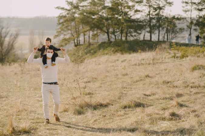 photo of man carrying his child on his back while standing on grass field